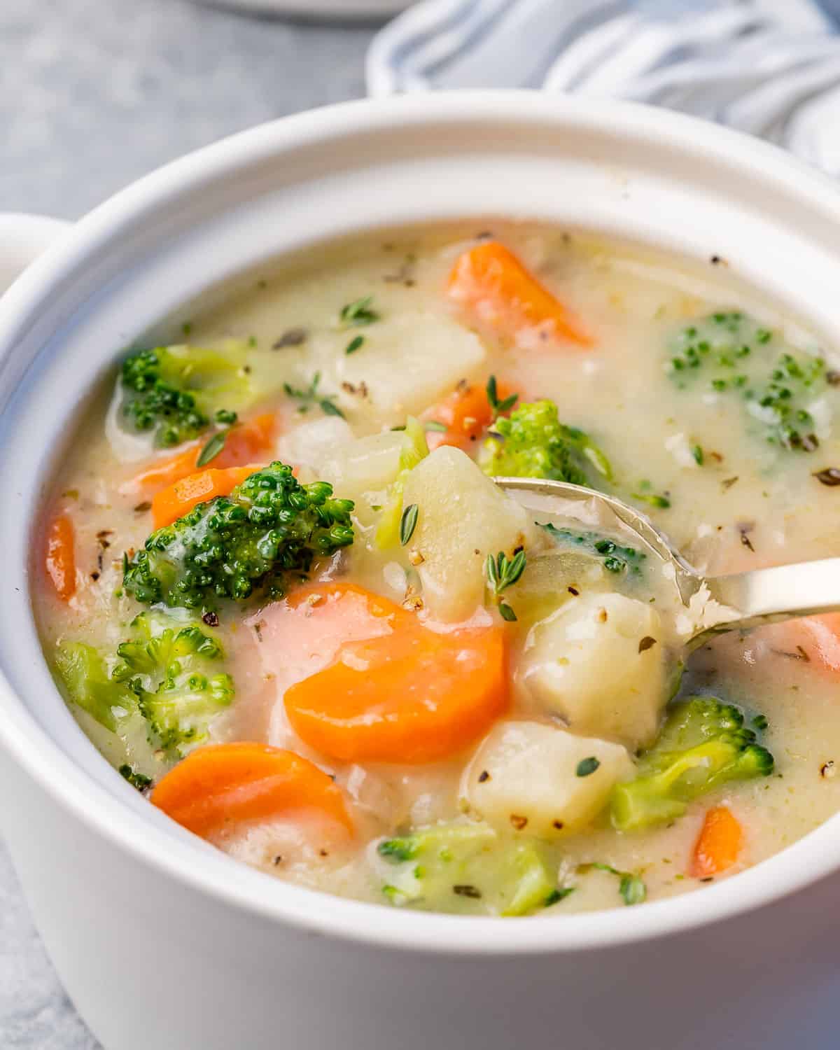 Close side view of a spoon stirring creamy vegetable soup in a white bowl.