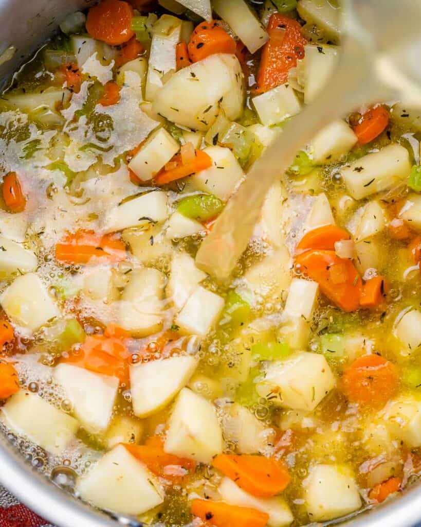 Adding broth to veggies in a soup pot.