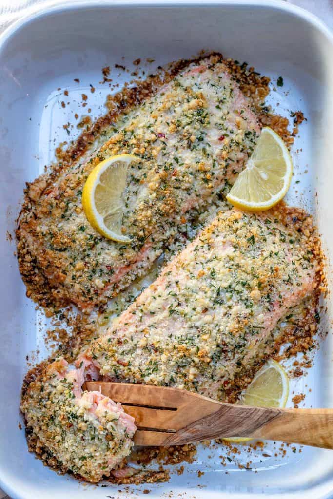 wooden spoon in a white dish that has two baked salmon filets, removing a piece of crispy baked salmon 