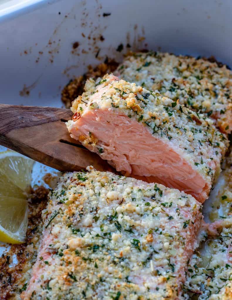 close up view of spoon removing a porting of baked crispy salmon from white dish