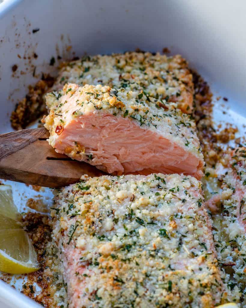 wooden spoon removing a piece of baked crispy salmon from the dish