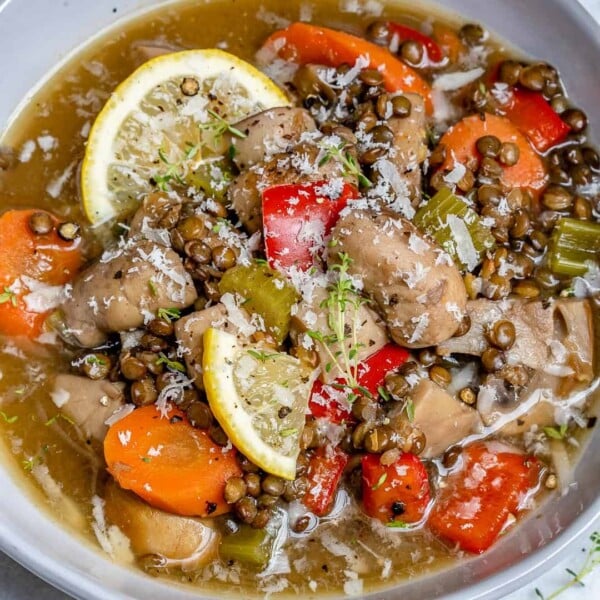 a bowl of soup made of lentil, mushroom, and carrots, topped with lemon garnishes.