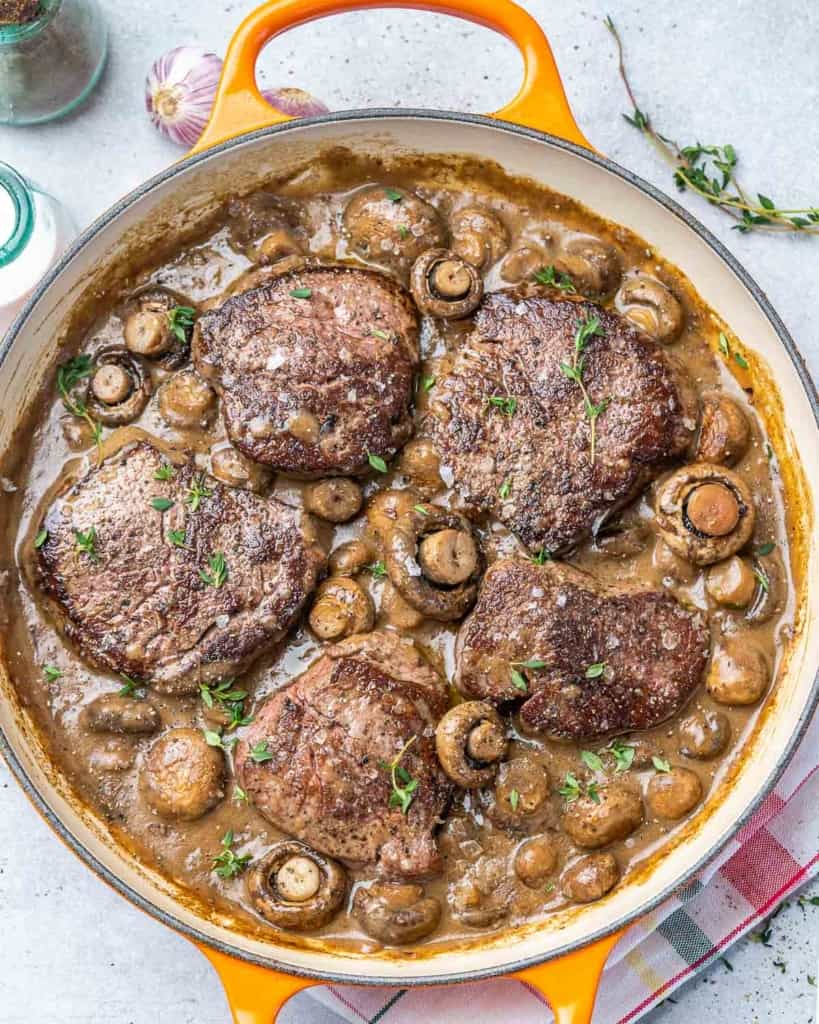 top view steak and mushroom in a yellow skillet