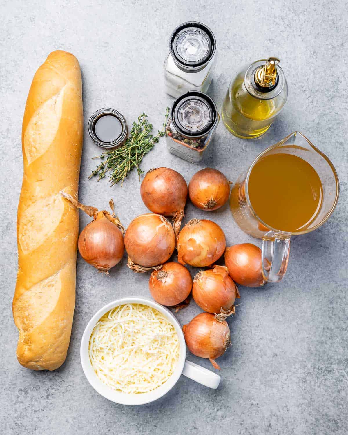 Baguette on a counter with onions, broth, thyme and grated cheese.