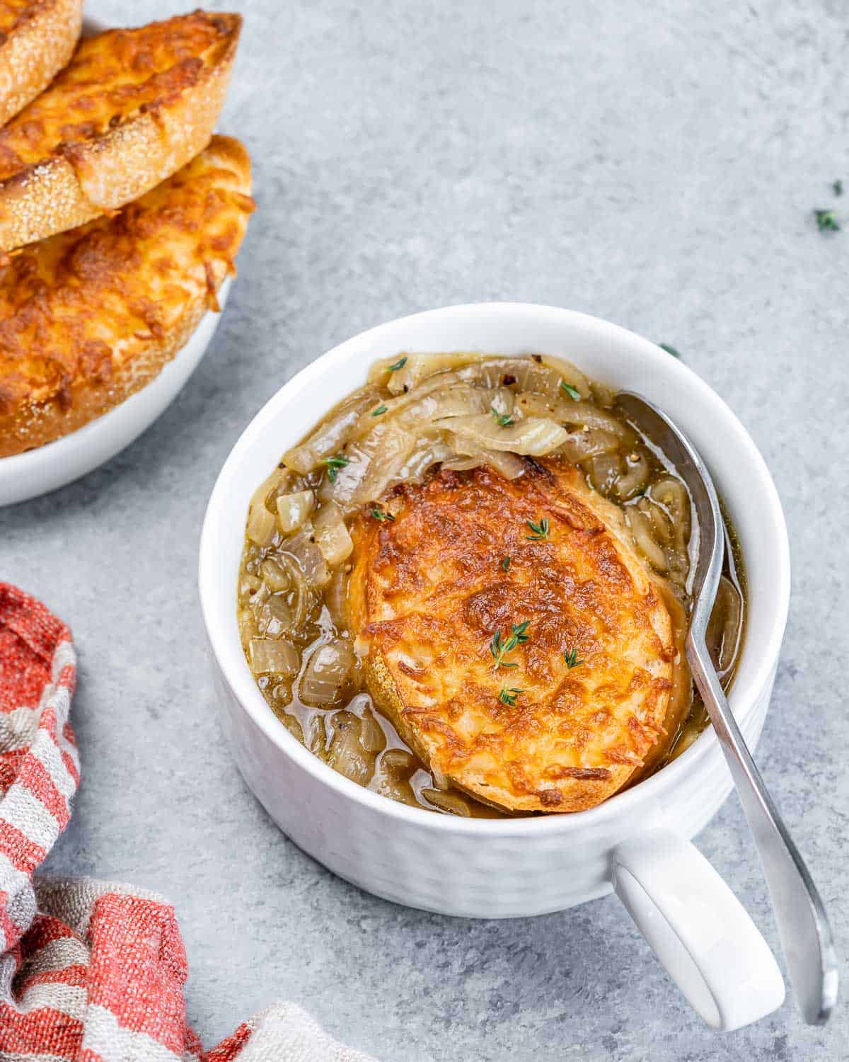 Spoon in a bowl of soup with onions and a toasted baguette. 