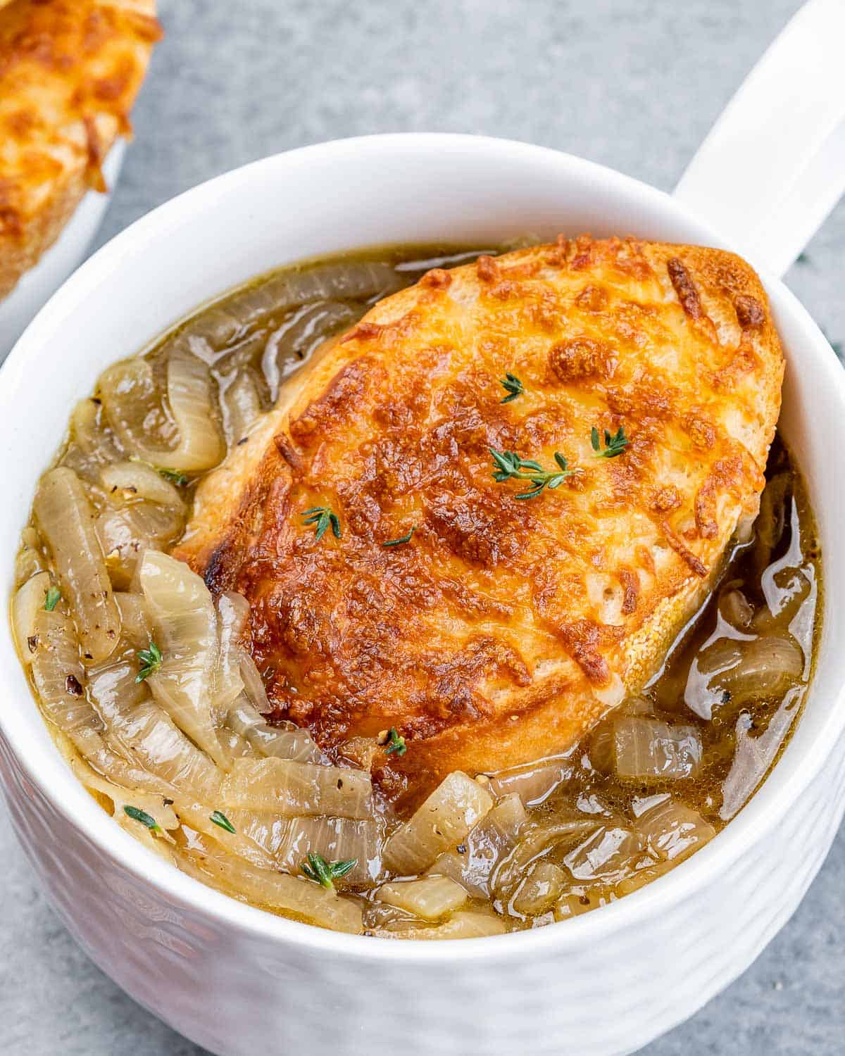 Closeup of French onion soup served with a cheesy toasted bread slice on top.