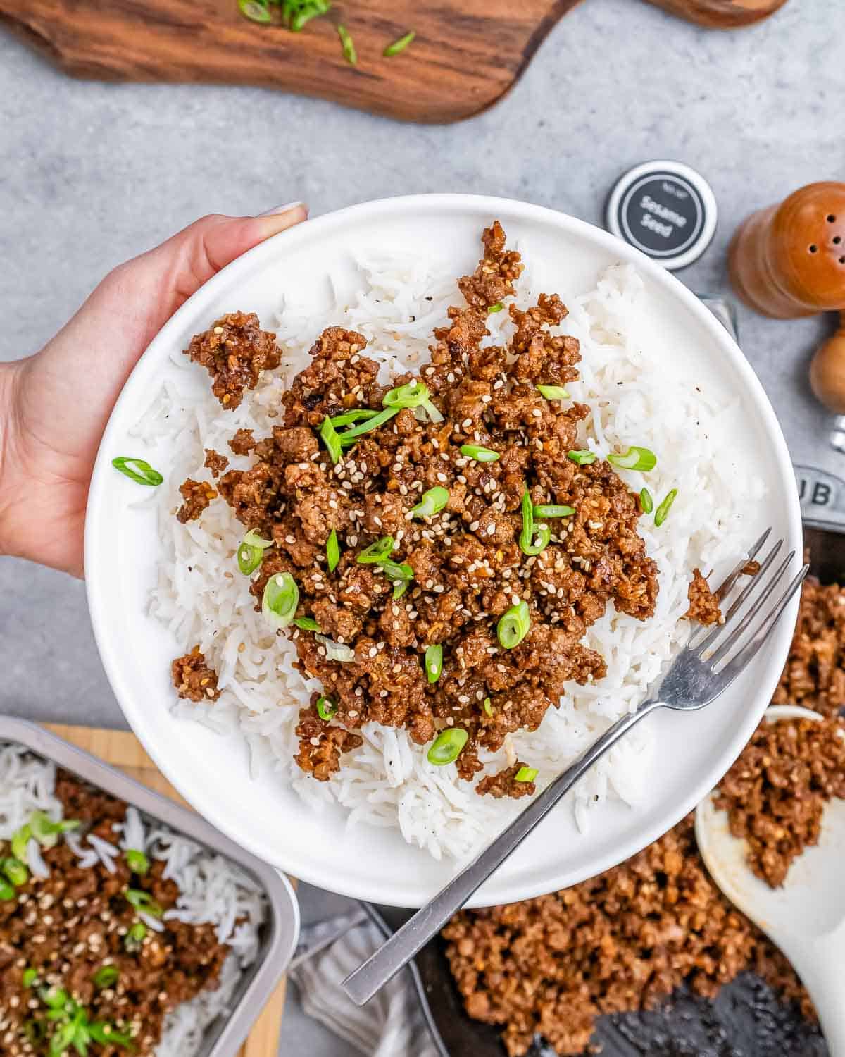 A hand holding a white plate with ground beef and rice with a fork on the side.