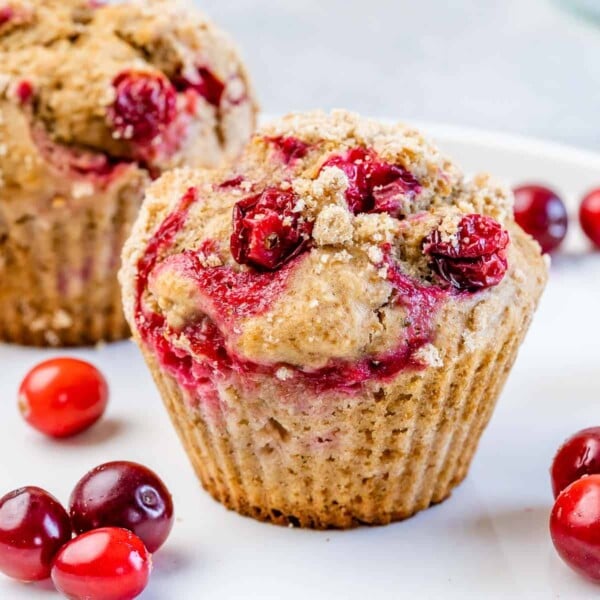 Side shot of a single muffin made with cranberries that are oozing from the muffin. On the side of the muffin there are a few fresh cranberries for imagery purposes.