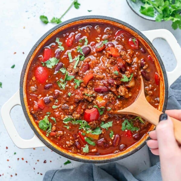 top view of a white pot with a wooden spoon grabbing some beef chili
