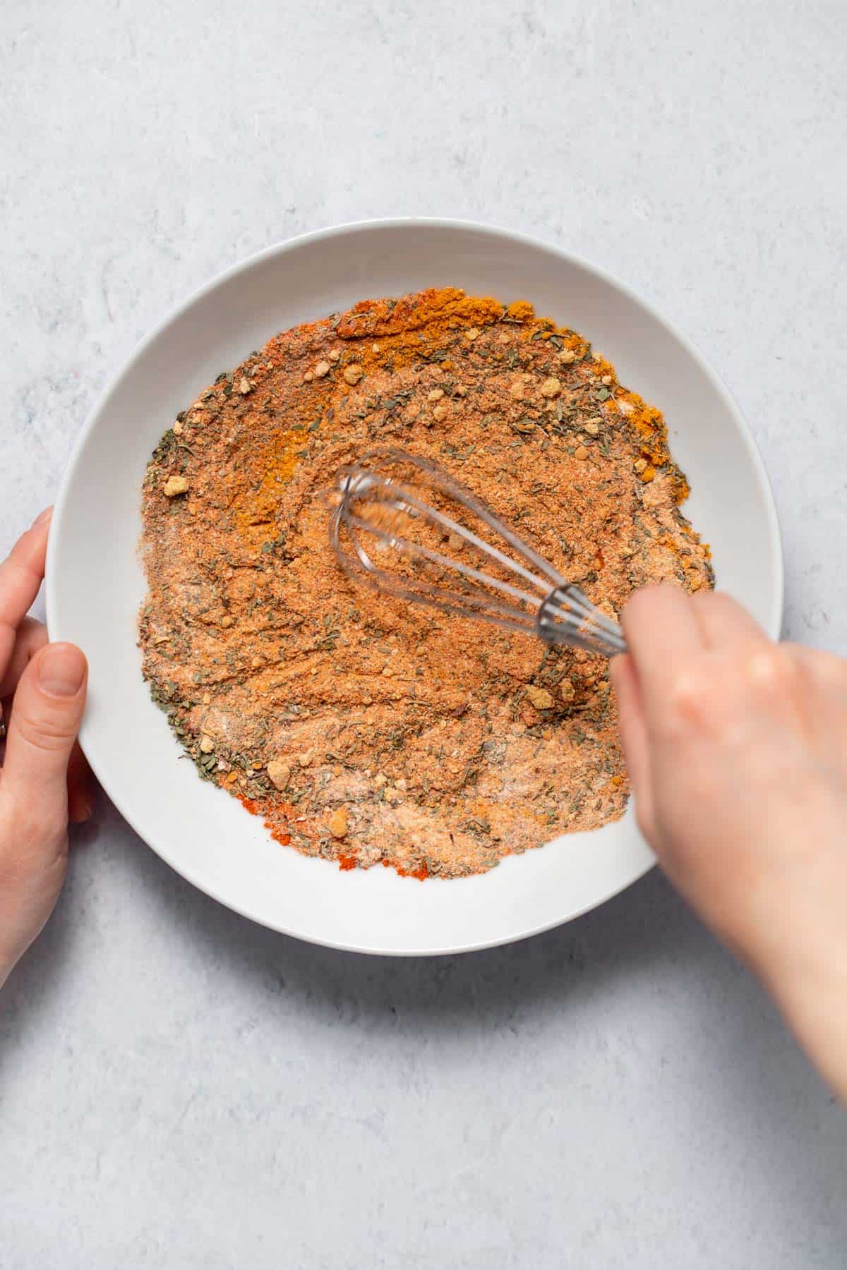 mixing spices and herbs in bowl with whisk