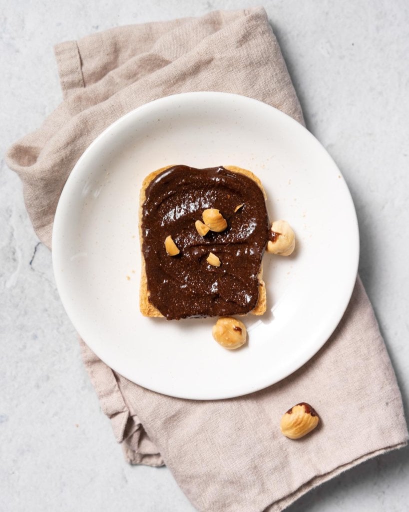top view of a plate with a toast of bread with Nutella spread topped with toasted hazelnuts