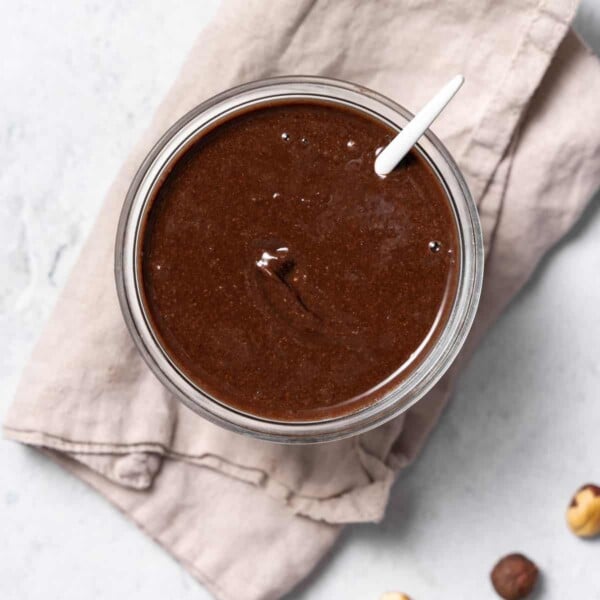 top view of a small bowl with brown colored homemade nutella with spoon in jar