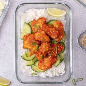 top view honey chicken over white rice and cucumber salad in a glass meal prep bowl