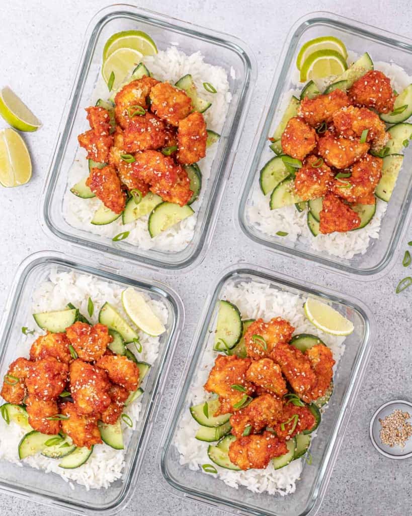 Meal prep bowls filled with honey sriracha chicken, rice and cucumbers.