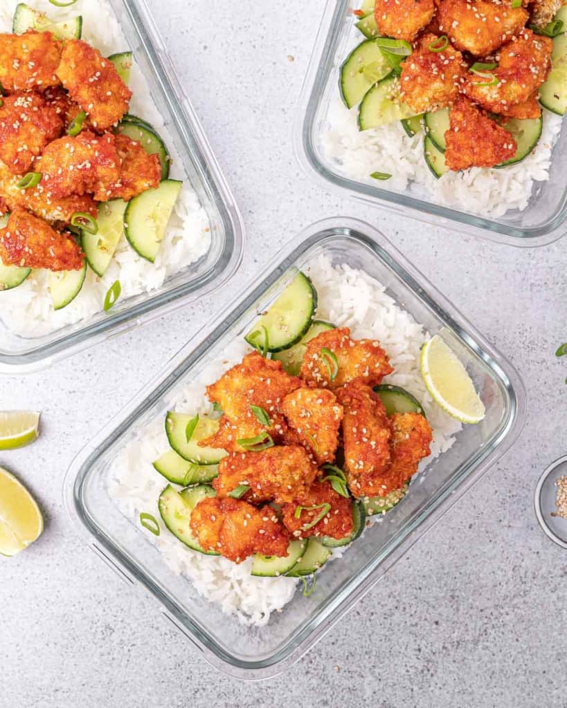 Honey chicken over white rice and cucumber salad in a glass meal prep bowl.