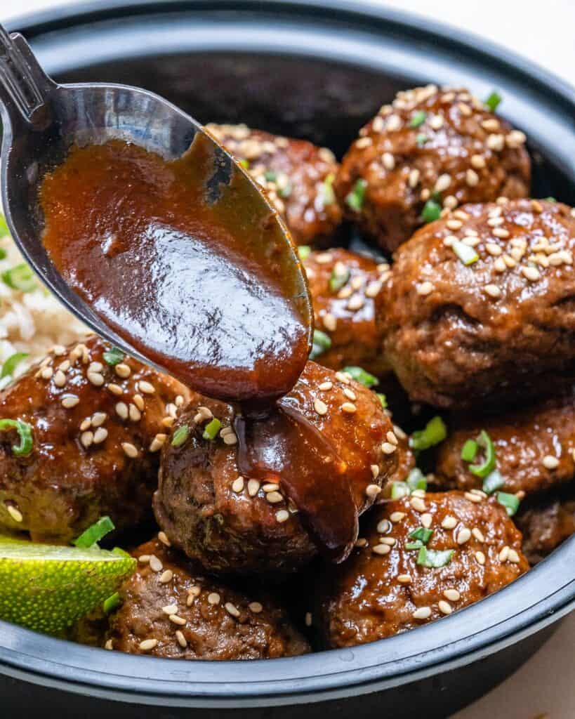 spoon pouring Asian sauce over meatballs