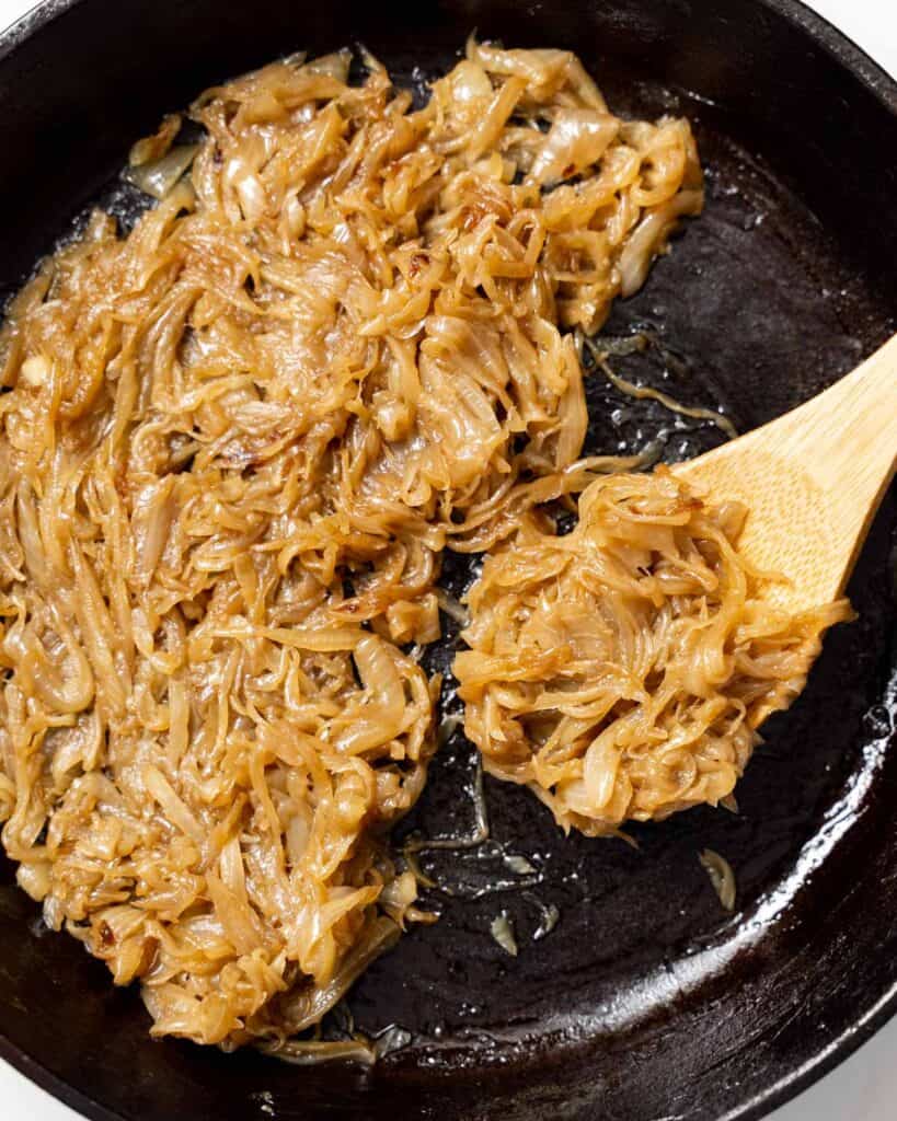 side shot of wooden spoonful of caramelized  onions in a black skillet