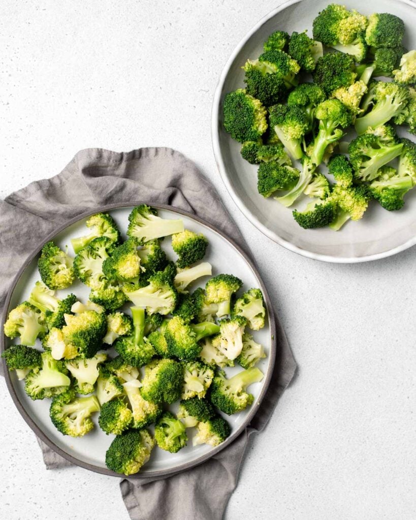 Plate full of broccoli florets next to a bowl filled with broccoli.