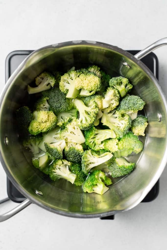 Adding broccoli florets to water in a pot.