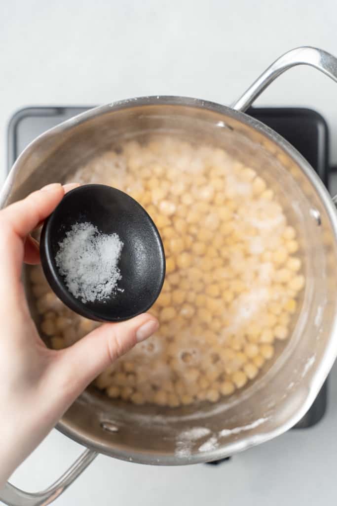 Adding salt to chickpeas in a pot of water.