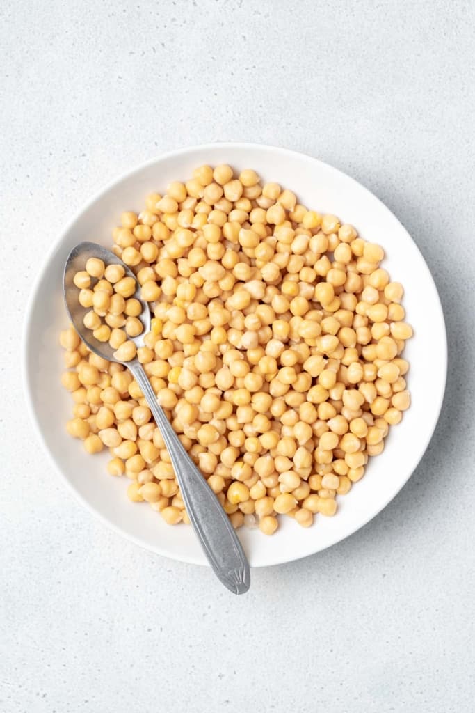Cooked chickpeas in a white bowl with a spoon.