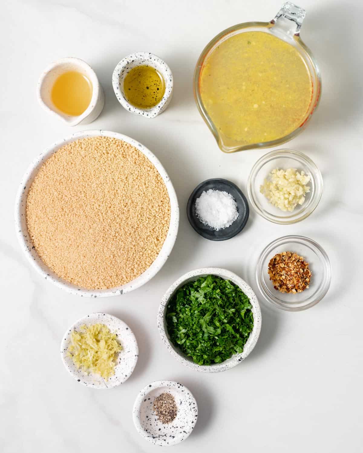 Uncooked couscous, parsley, broth, salt, garlic and olive oil in small bowls.