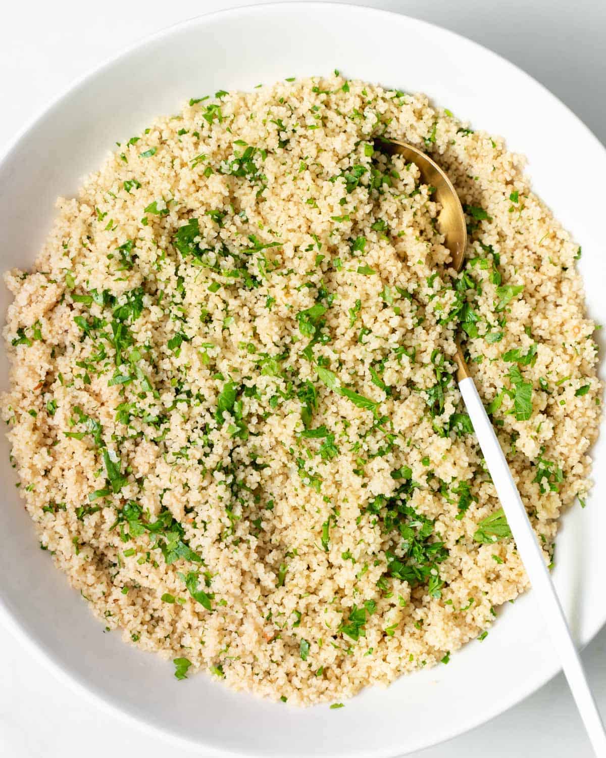 Top view of a round plate of cooked couscous with chopped parsley and spoon on plate over couscous.