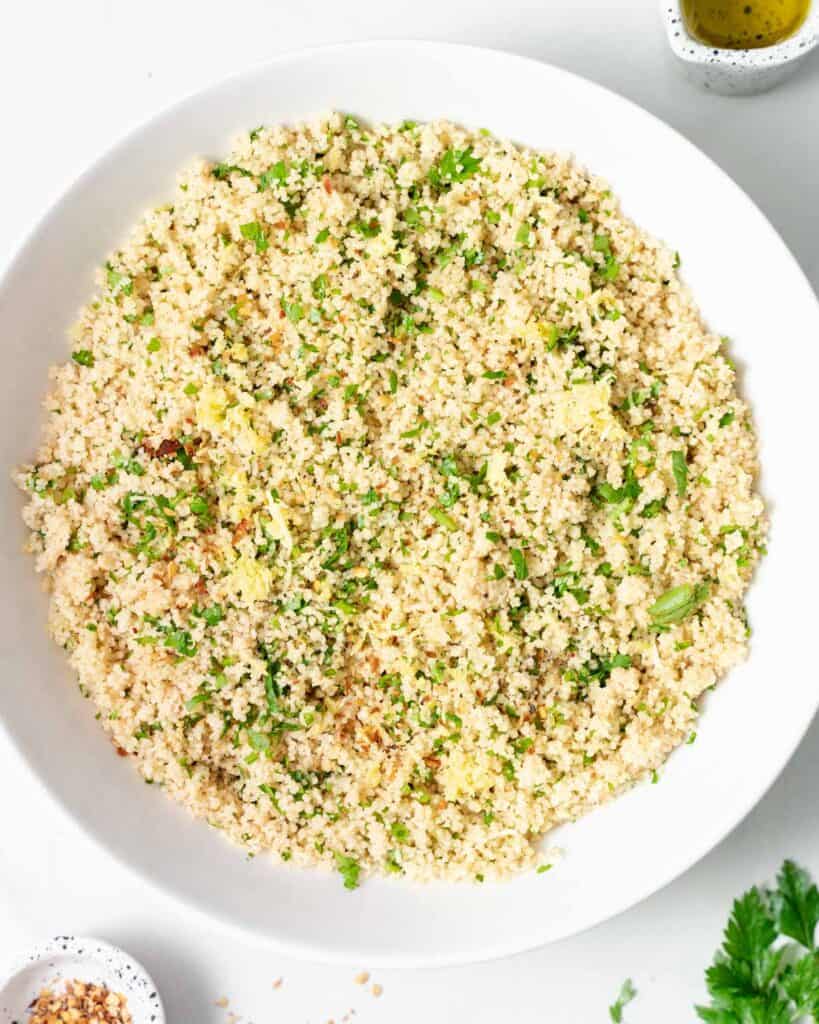 Couscous in a white bowl with the addition of parsley.