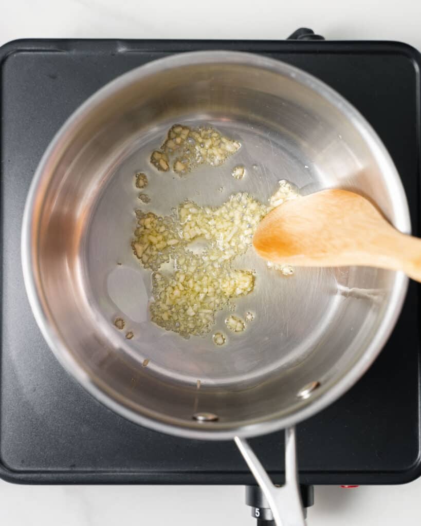 Using a wooden spoon to stir garlic in a pot with oil.