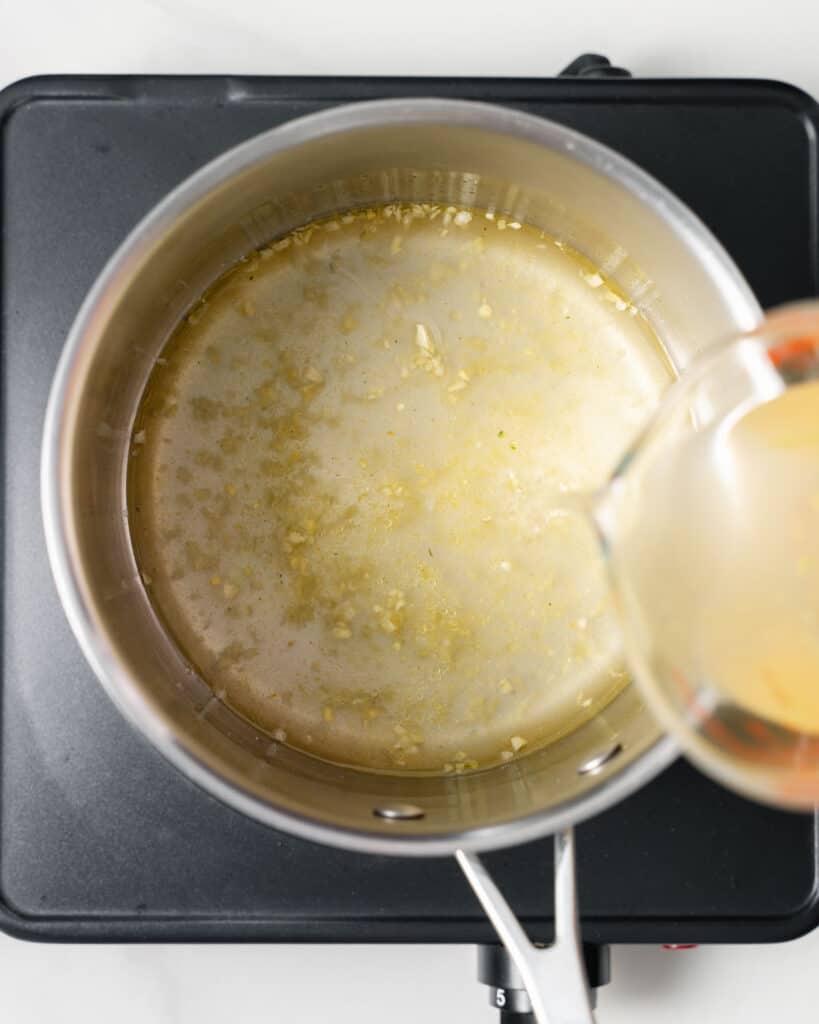 Pouring broth in a large pot with sautéed garlic.