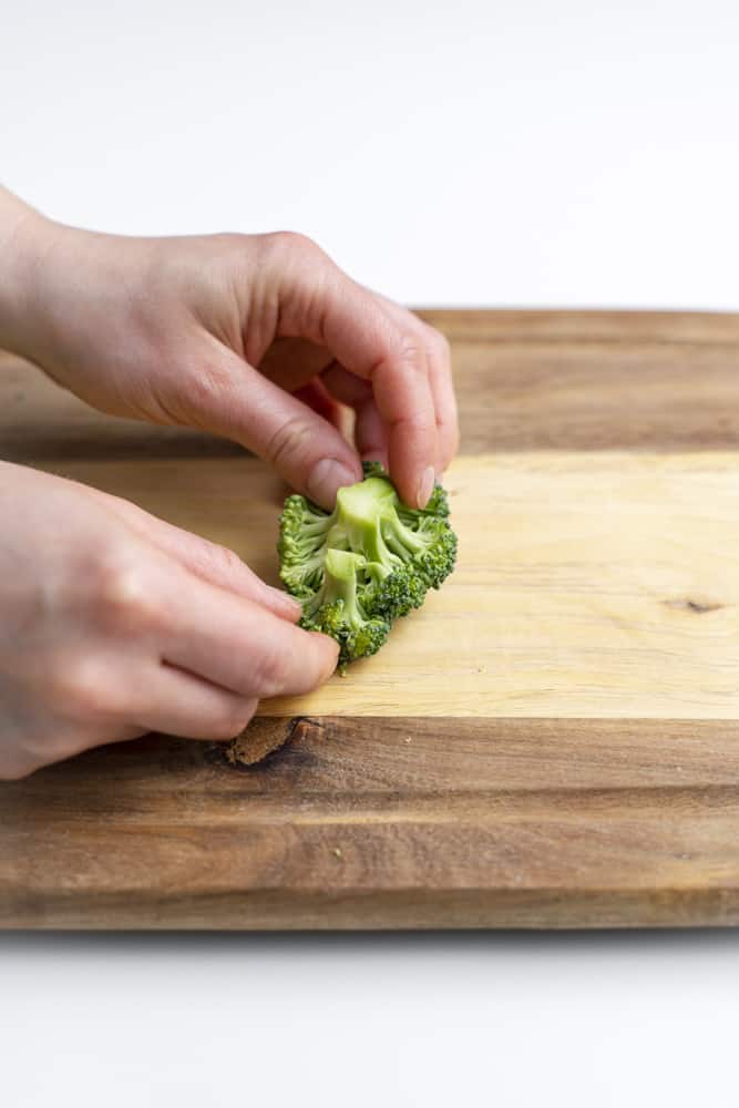 Hands holding two very small broccoli florets.