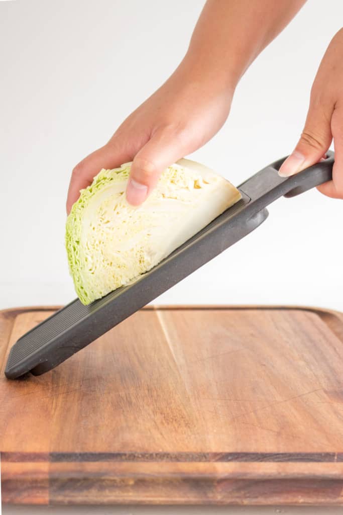 hand holding cabbage over mandolin