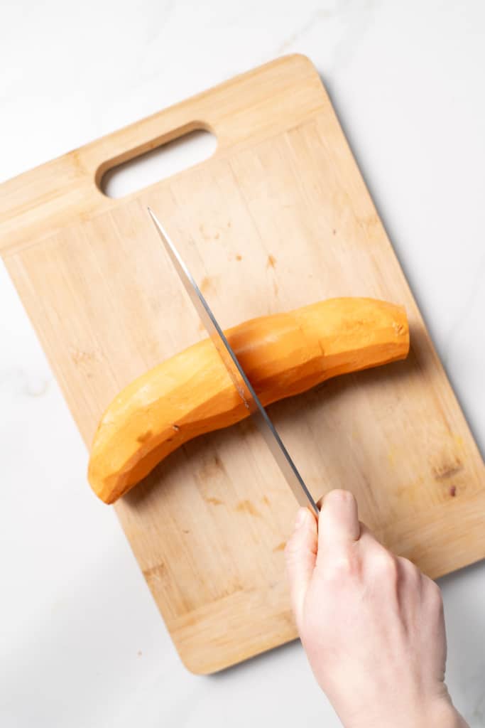 Cutting a peeled sweet potato in half.