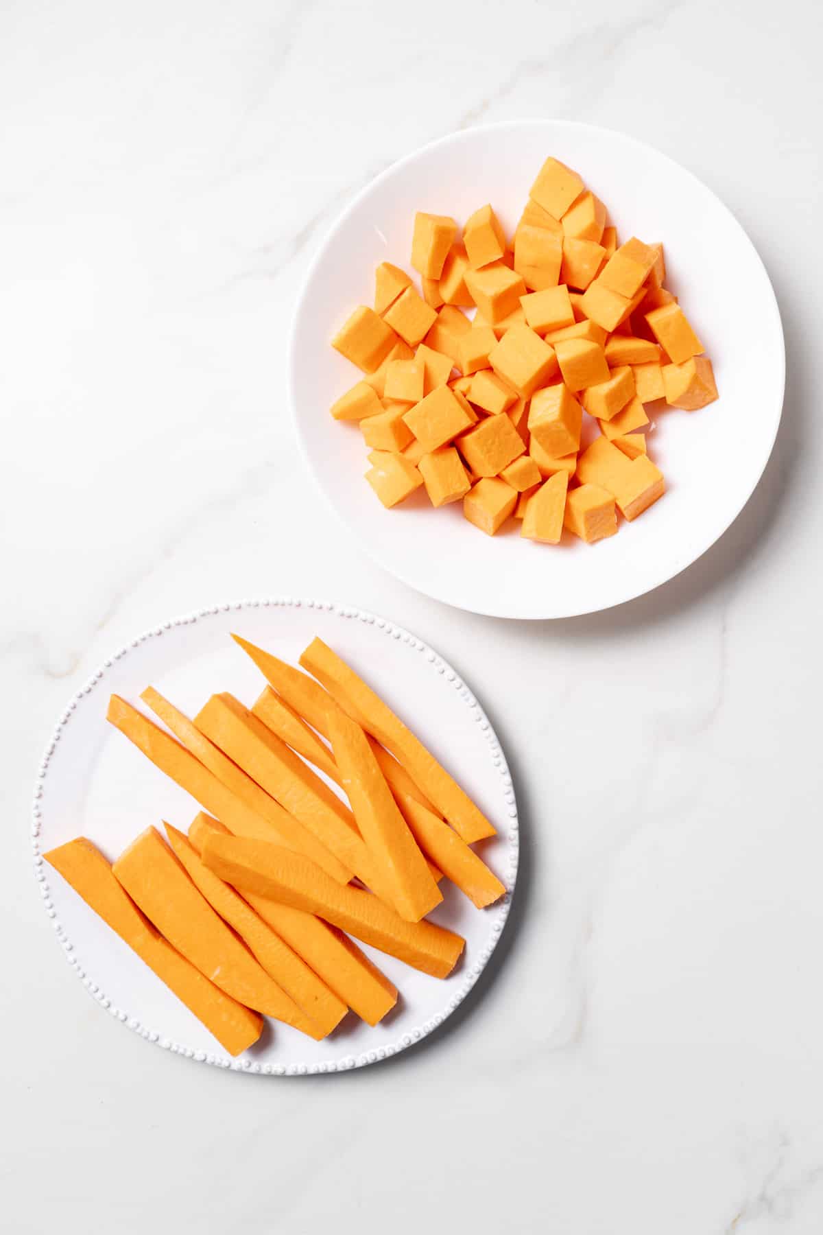 Sweet potato cut into cubes and sticks on two white plates.