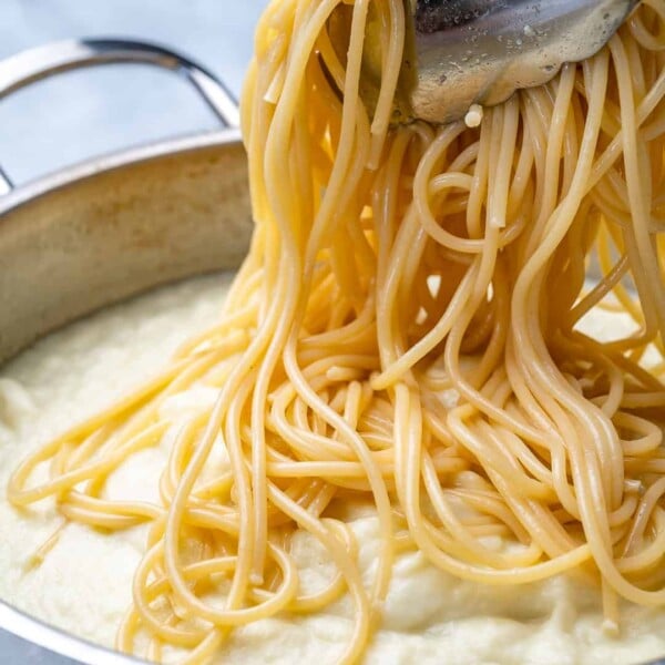 spaghetti being added over alfredo sauce in pan