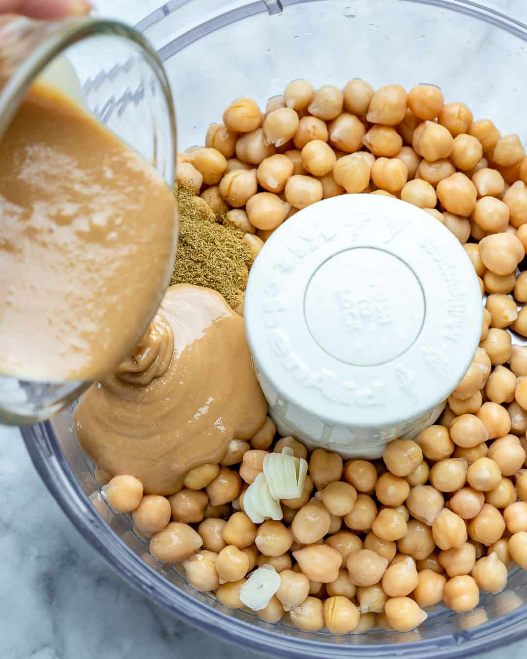 chickpeas added  in the blender for hummus and tahini is being poured into the blender.