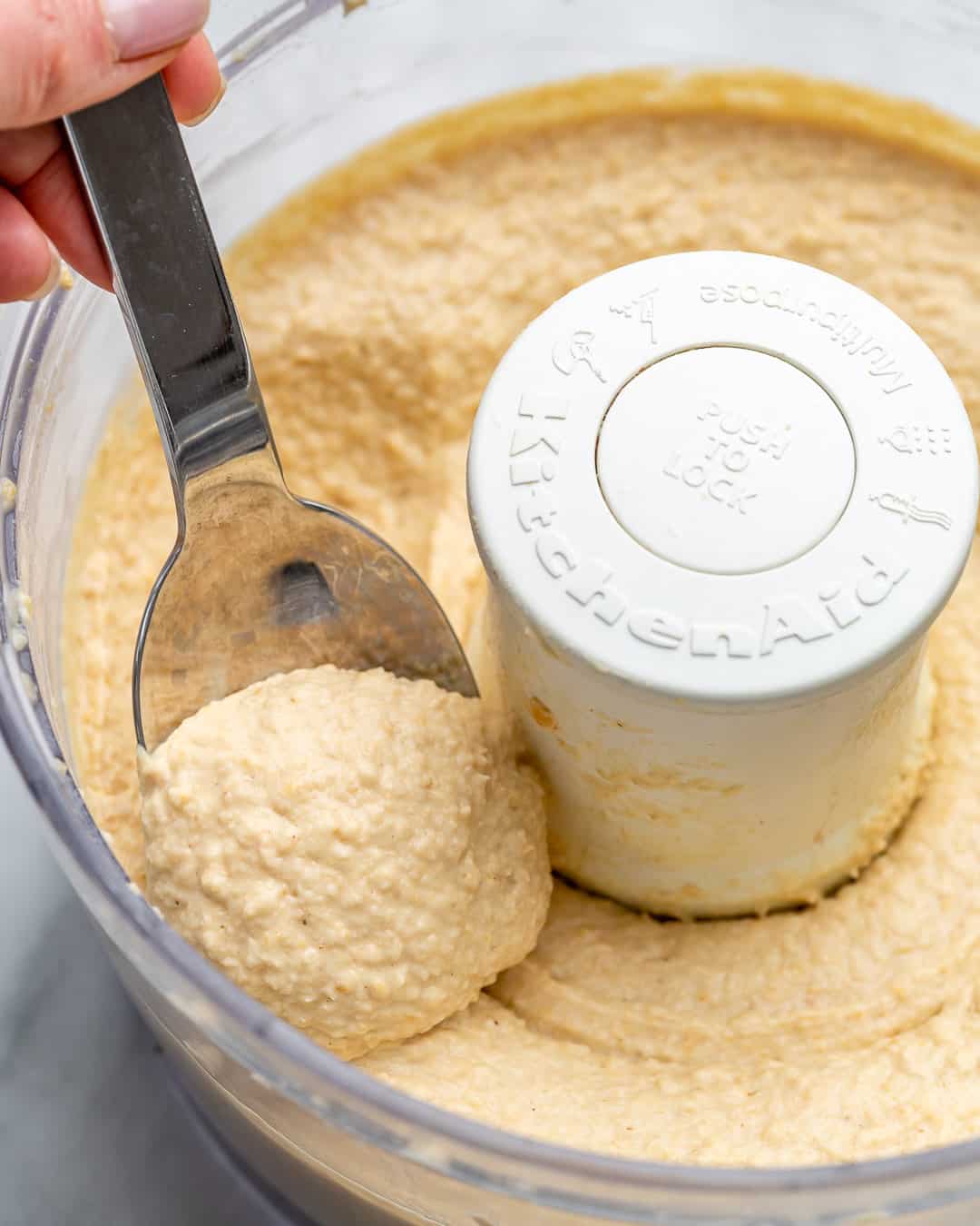 Spoon, removing blended hummus from the food processor.