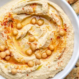 homemade hummus in a white dish with a drizzle of olive oil, chickpeas, and paprika.
