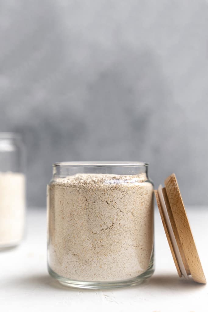 side shot of a jar with oat flour in the jar and a lid on the right of the jar