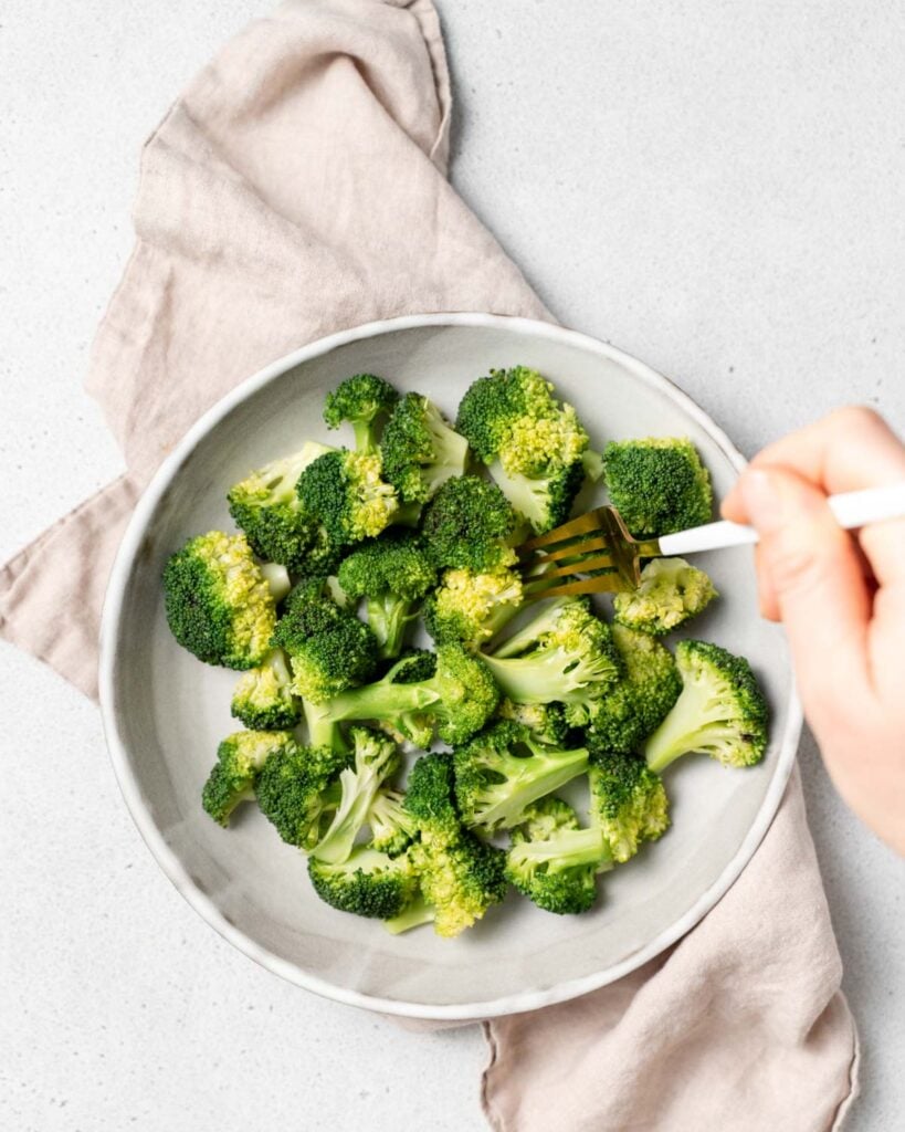 hand holding fork grabbing a piece of cooked broccoli floret from a plate
