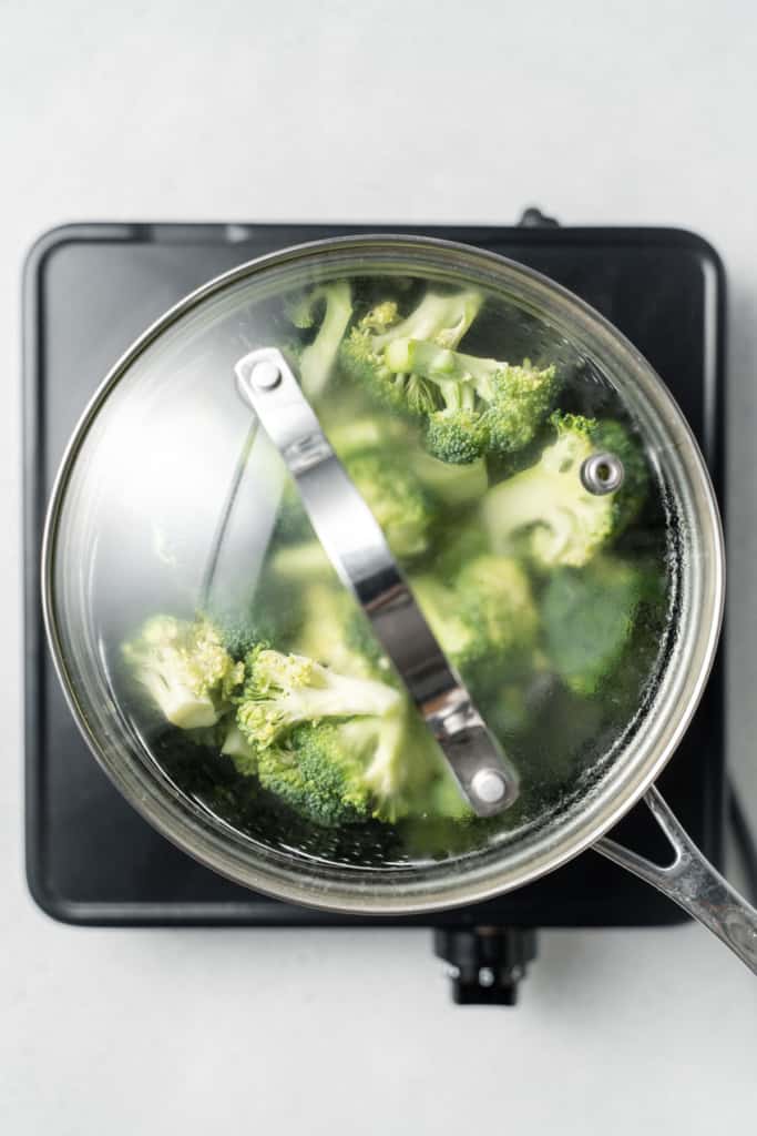 Broccoli florets steaming in a covered pot.