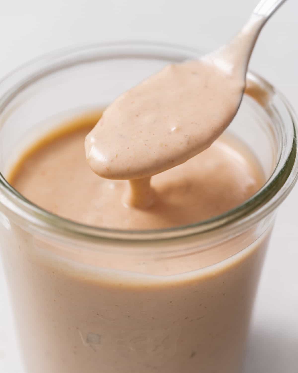 Getting a spoonful of In-N-Out sauce out of a glass jar.