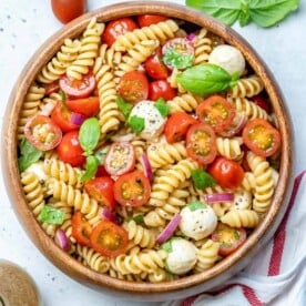 Caprese pasta salad in a round wooden bowl topped with fresh basil.