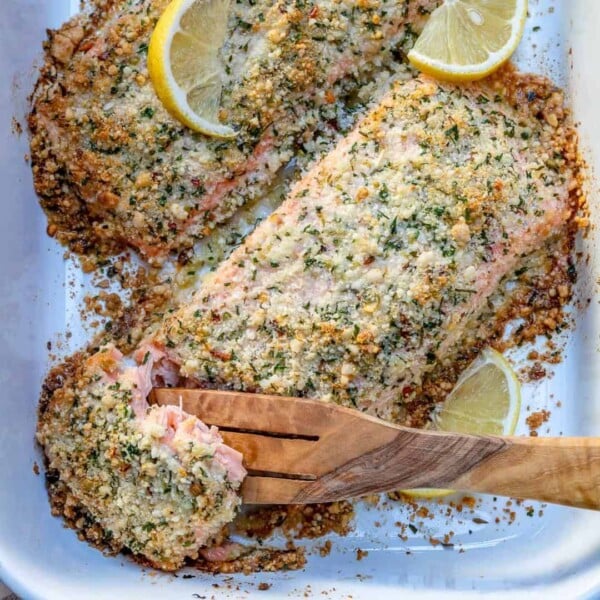 a wooden spoon grabbing a piece of baked salmon crusted with parmesan from a dish.