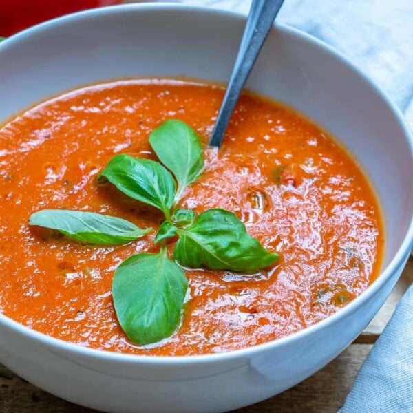 a bowl with red fresh homemade tomato soup with fresh basil and spoon in bowl.