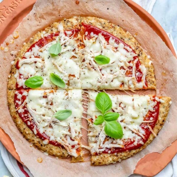 Cauliflower crust pizza cut into 4 slices and topped with melted cheese and sliced fresh tomatoes.