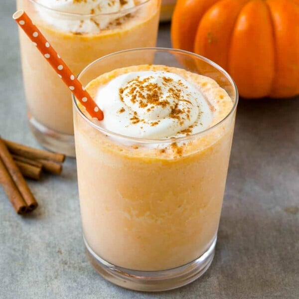 an orange looking pumpkin pie protein shake in a cup topped with whipped cream and a dash of cinnamon.
