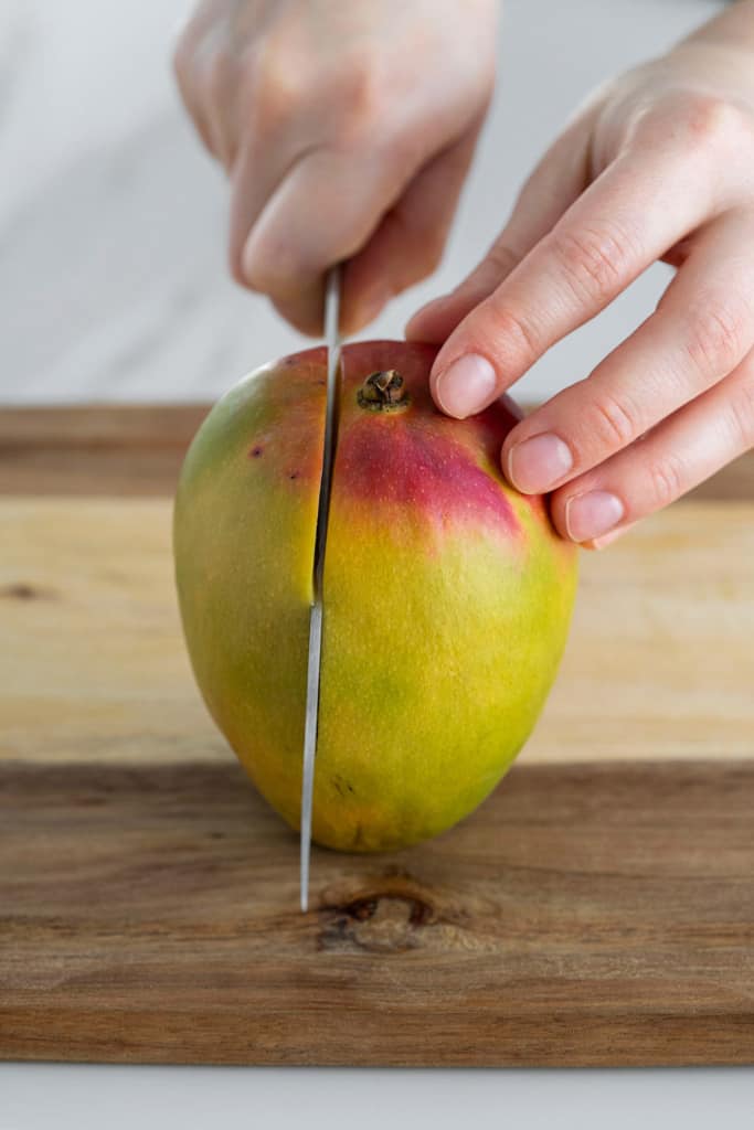 mango stem side up with knife slicing flesh side down
