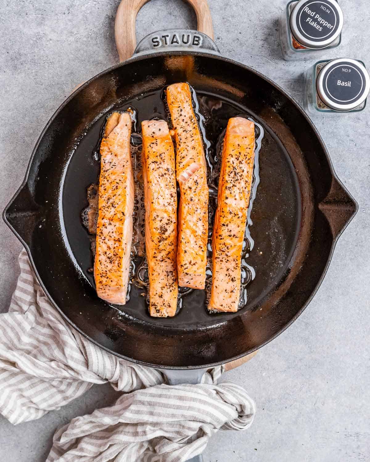 4 seared salmon fillets on a black skillet.
