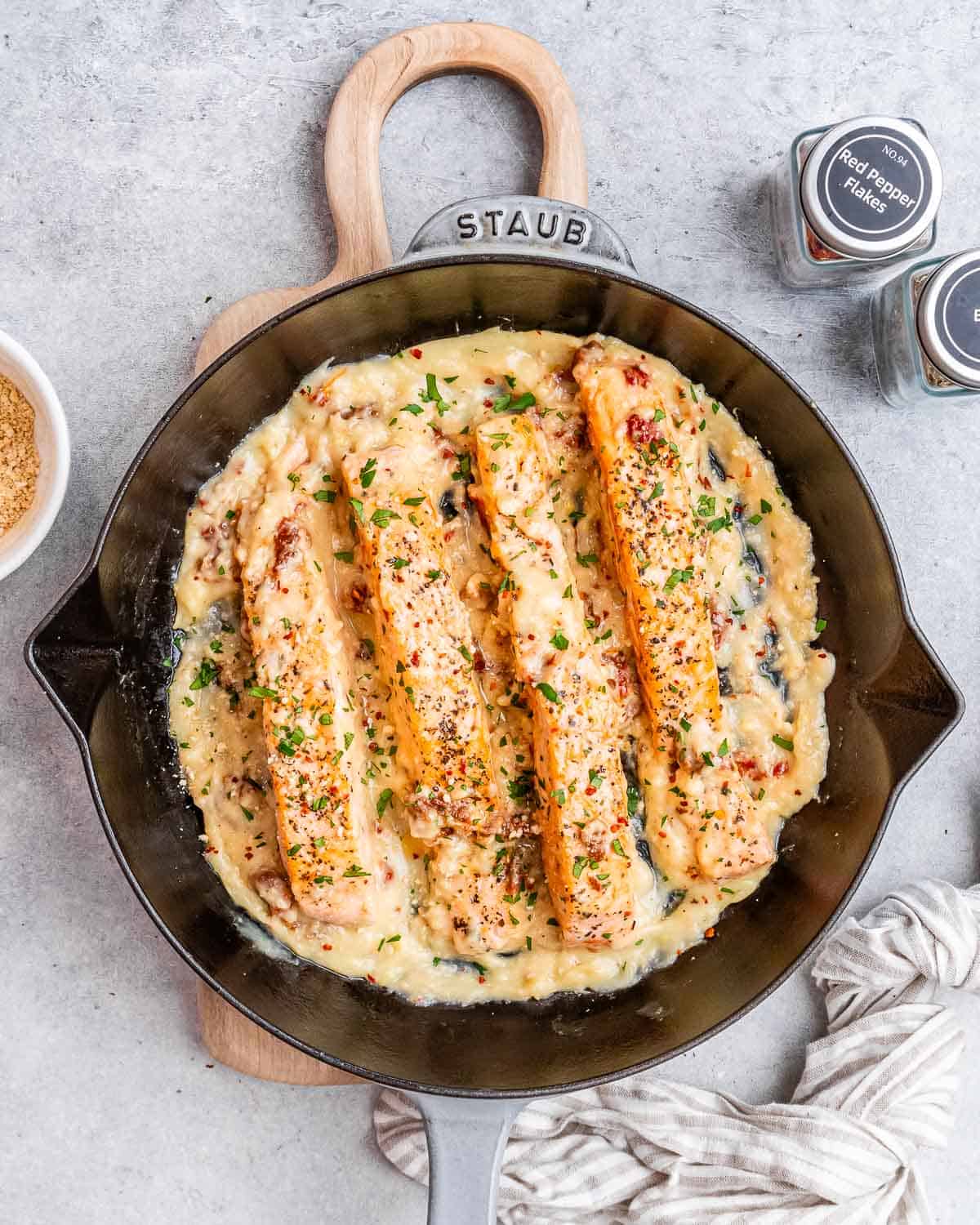 a black skillet with 4 salmon fillets in a creamy sauce.